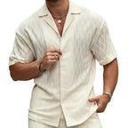 Man wearing a light-colored shirt and pants against a stone wall.