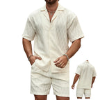 Man wearing a beige linen shirt and shorts set against a stone wall.