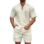 Man wearing a white textured shirt and shorts set against a stone wall.