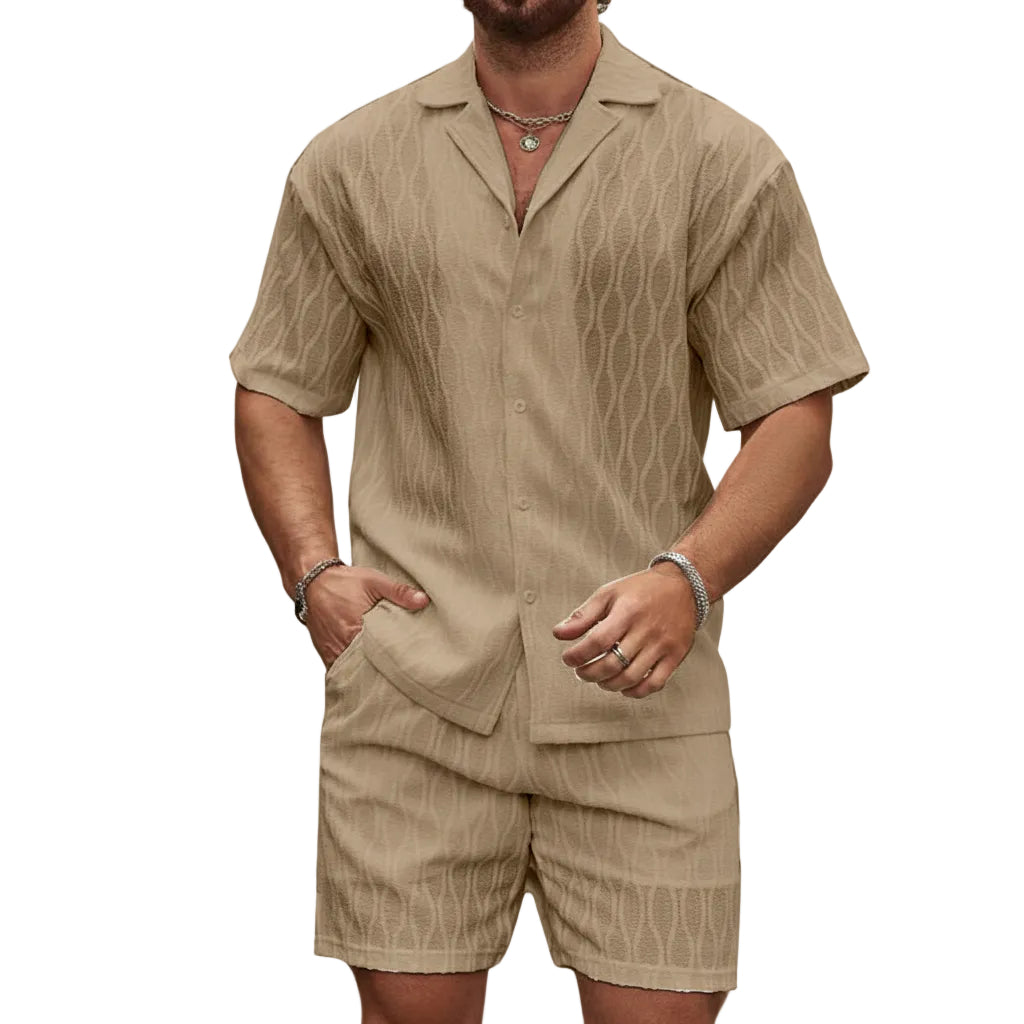 Man wearing a beige button-up shirt and shorts set against a stone wall.
